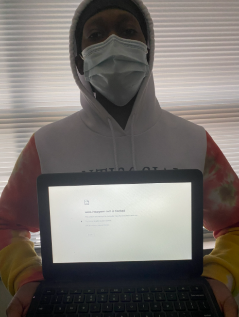 A student holding a chromebook with a blocked site. 